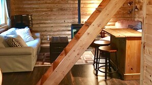 Ein gemütliches Blockhaussinnenzimmer mit einer Holztreppe, einer Couch, einem kleinen Tisch und einer Bar.