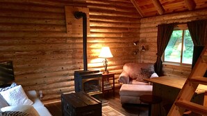 Ein gemütliches Blockhaus-Interieur mit Kamin, einer Couch, einem Sessel und einem kleinen Tisch.