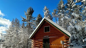 Eine Blockhütte mit grüner Tür, auf der "Summer Haven" steht, umgeben von schneebedeckten Bäumen.