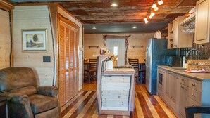 A cozy kitchen with wooden floors, a dining area with chairs, and a refrigerator. - Rustic Cabin - Jetted Tubs - Wi-Fi - Wonderful Views - Grill - Firepit - Porch (Makanda)