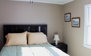 A bedroom with a large bed, two pillows, a bedside table with a lamp, and two framed pictures on the wall.