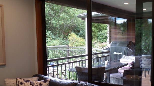 A modern living room with a leather sofa, a glass coffee table, and a view of a patio area with outdoor furniture and a barbecue grill.