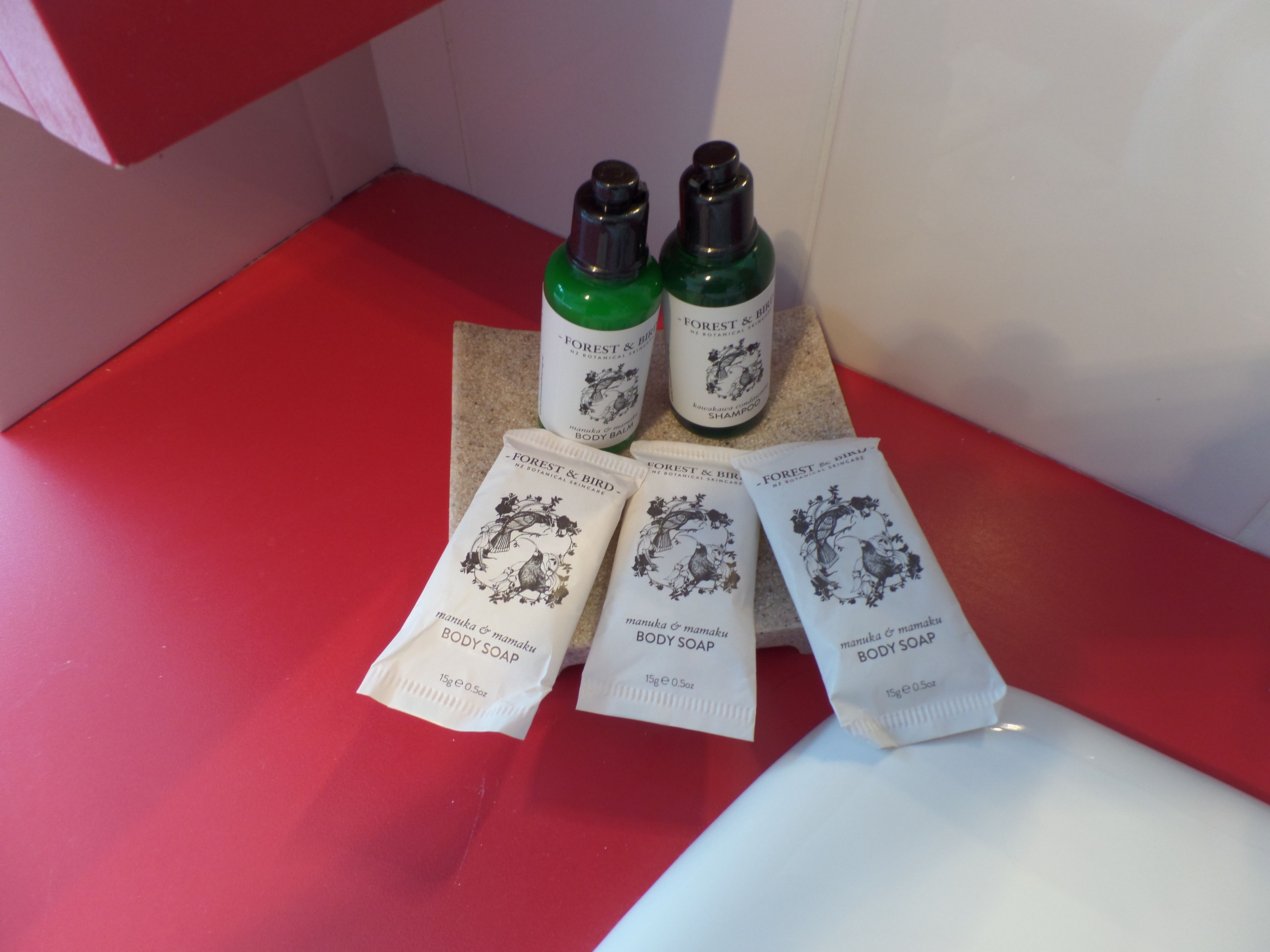 Un plan de travail rouge sur lequel sont disposés trois flacons de produits de soins corporels de la marque Forest & Bird et quatre sachets de savon pour le corps.
