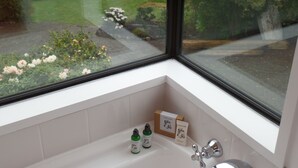 A bathroom with a window overlooking a garden. There are two bottles and two boxes on the sink counter.