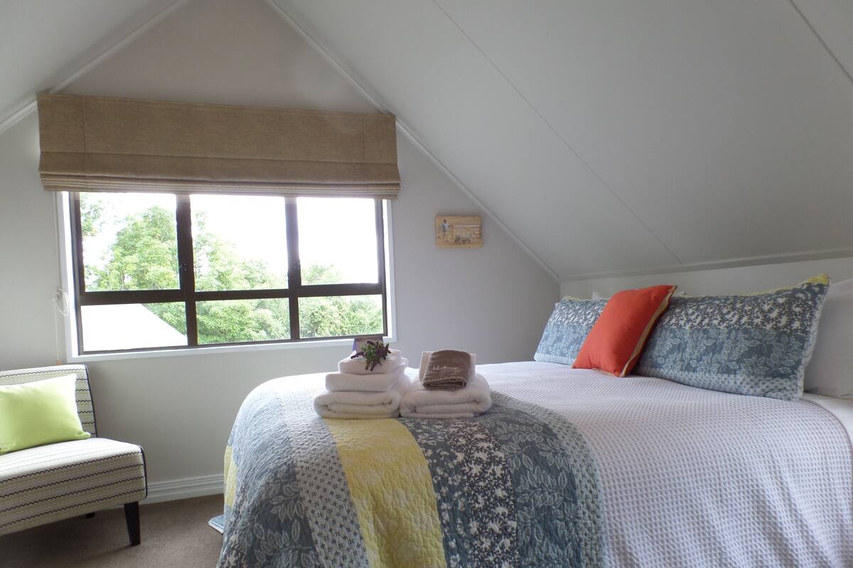 A bedroom with a bed, a window, a chair, and a bedside table.