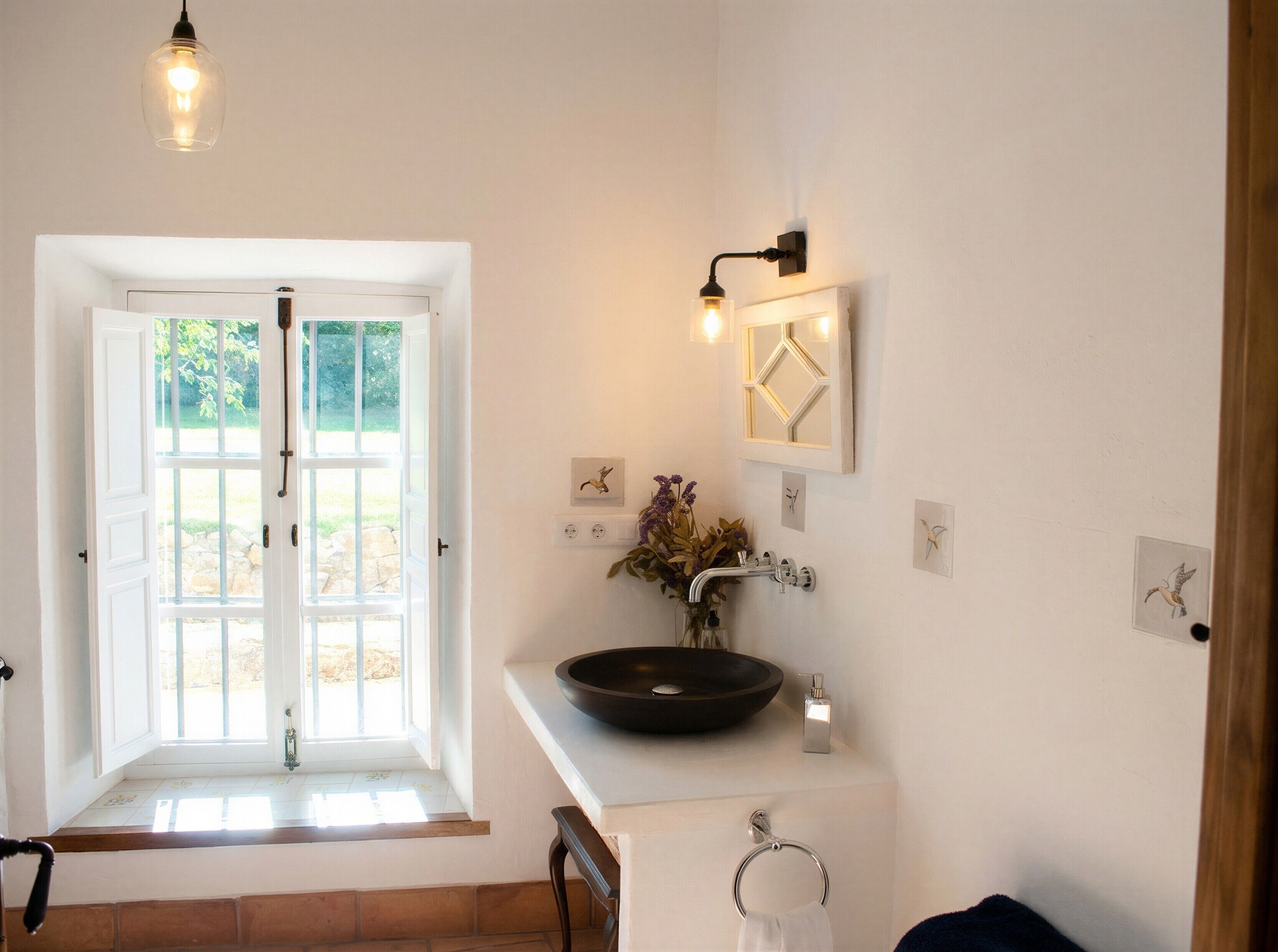 A bathroom with a large window, a vessel sink, and a wall-mounted light fixture.