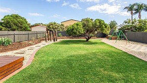 A backyard with a wooden deck, a lawn, a tree, and a swing set. - Sea Devine (Port Willunga)
