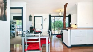 A modern kitchen with white cabinetry, a dining area with red upholstered chairs, and a large window offering a view of the outdoors. - Sea Devine (Port Willunga)