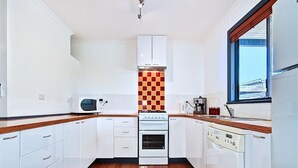 A compact kitchen with white cabinets, a microwave, an oven, and a dishwasher. - Sea Devine (Port Willunga)