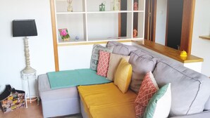 Ett vardagsrum med en soffa, en lampa, en hylla med dekorativa föremål och ett litet bord.