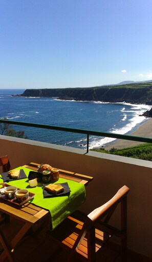 Une table dressée avec de la nourriture et des boissons sur un balcon donnant sur une vue côtière, avec des falaises et l’océan.