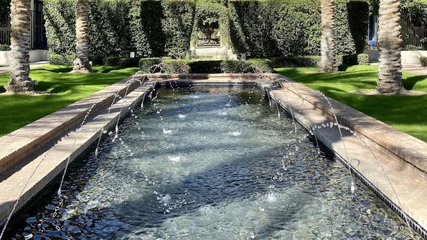 Une piscine à l’eau claire, entourée de palmiers et bordée d’un bâtiment doté de balcons.