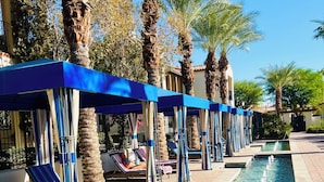 Un espace piscine agrémenté de chaises longues et de parasols, entouré de palmiers.