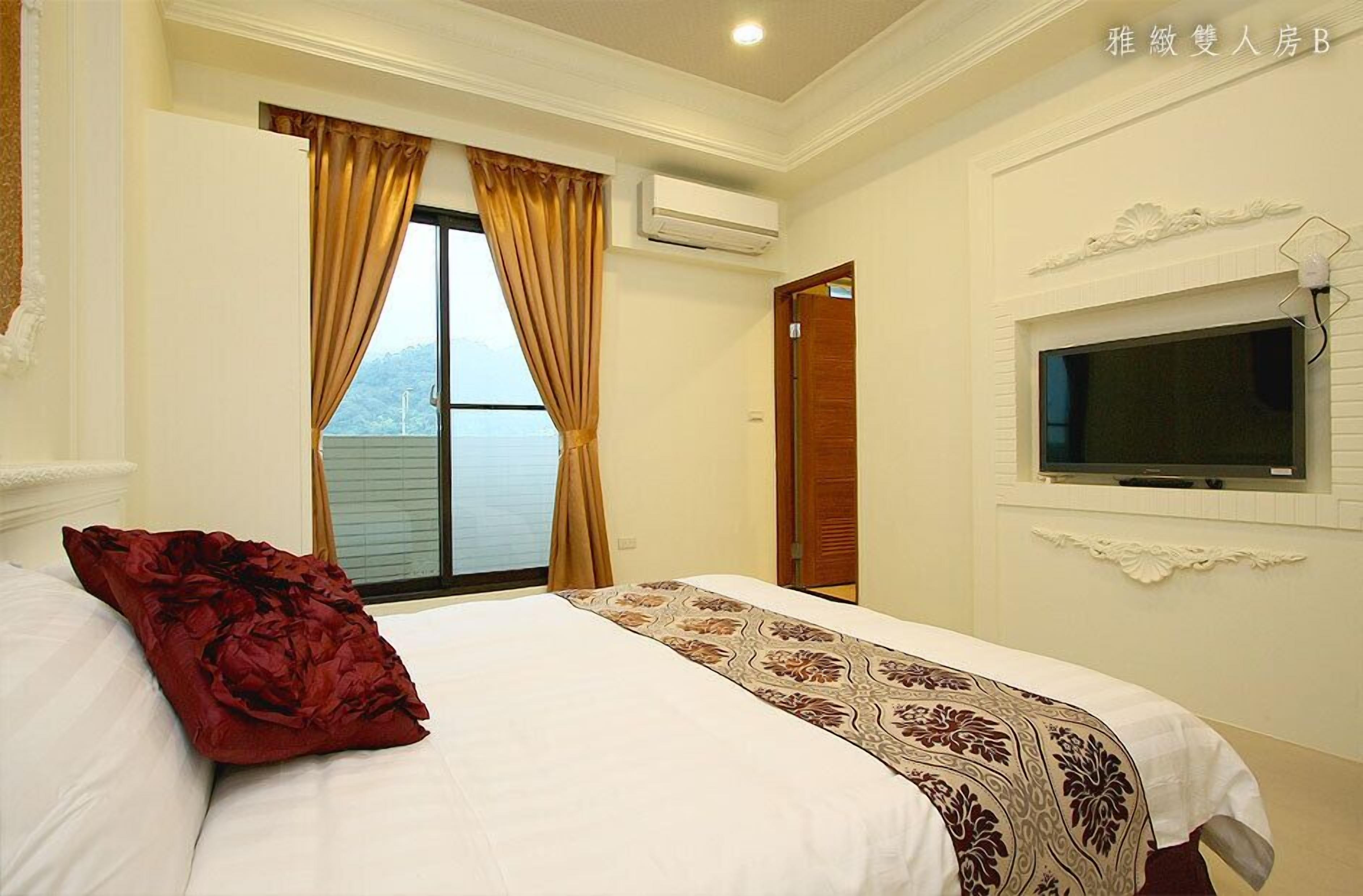 A hotel room with a bed, a TV mounted on the wall, and a window with curtains.