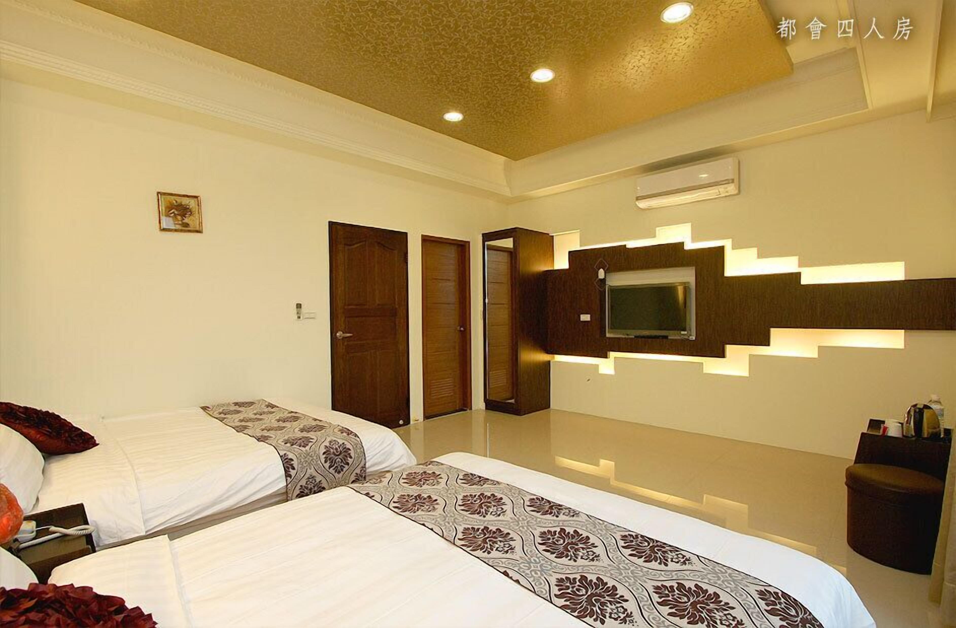 A hotel room with two beds, a TV mounted on the wall, and a staircase leading to another room.