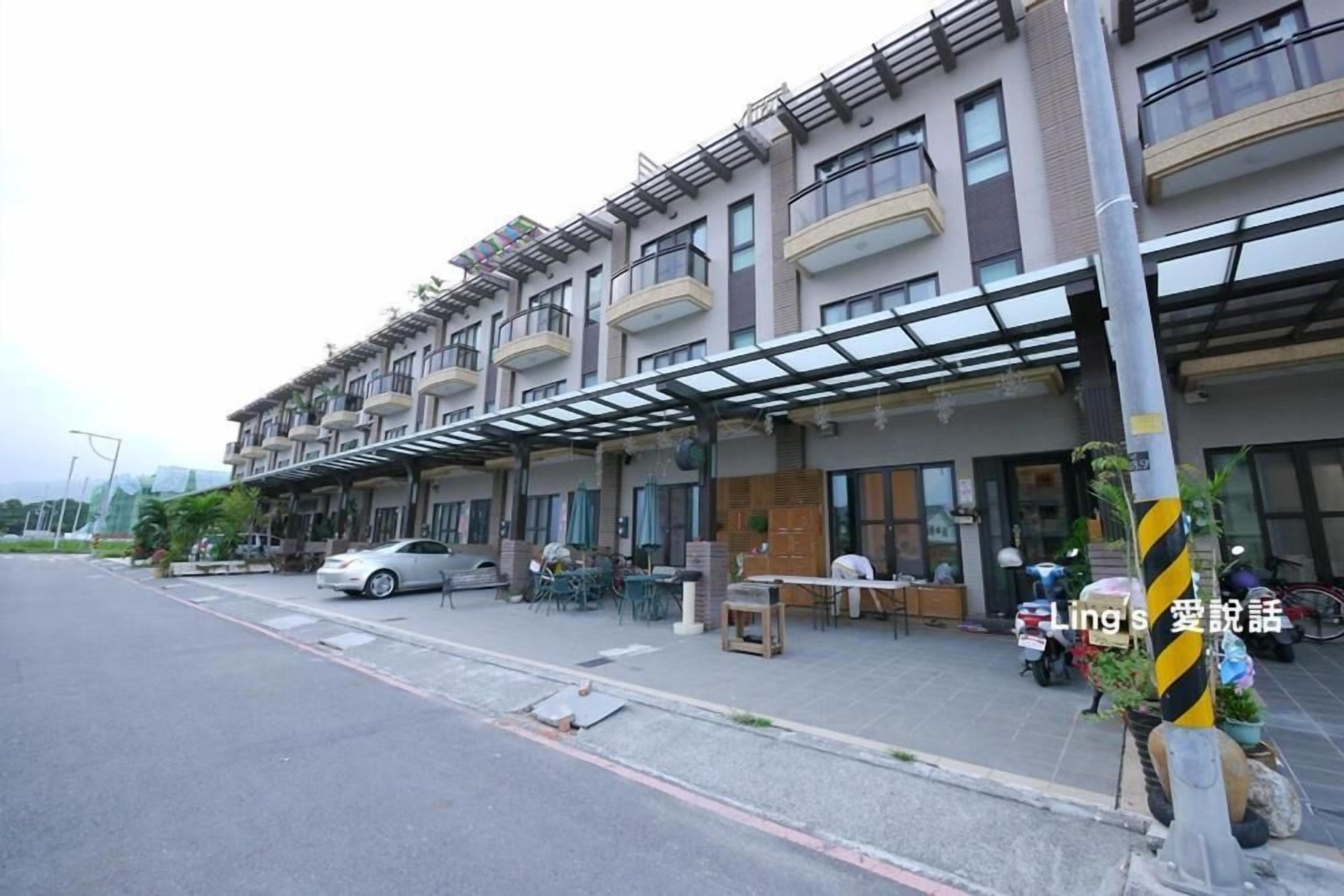 A multi-story residential building with balconies, a covered outdoor seating area, and a street view.