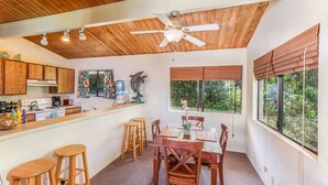 Eine Küche mit Holzausstattung, ein Essbereich mit Tisch und Stühlen, ein Deckenventilator und ein Fenster mit Jalousien.