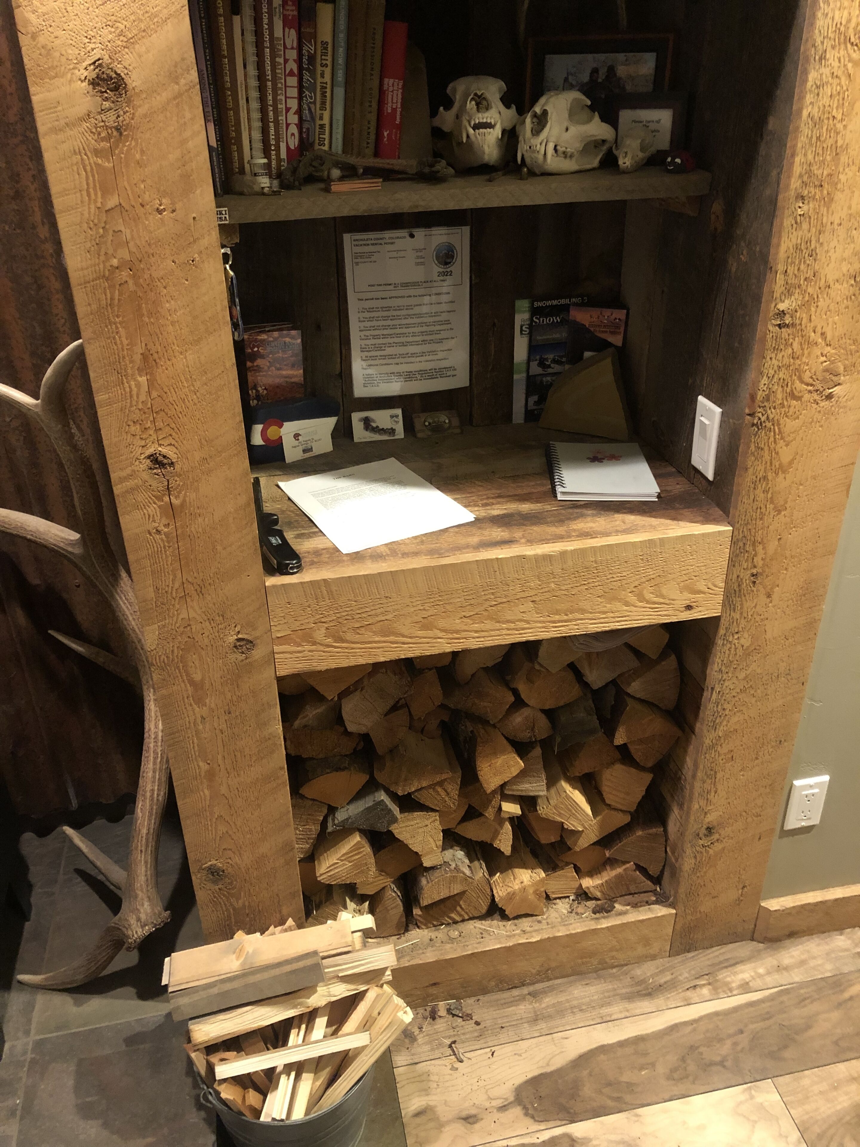 Un escritorio de madera con un estante que contiene libros y calaveras, un certificado enmarcado y un bloc de notas.