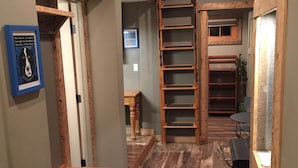 Un pasillo estrecho con suelo de madera, un banco de madera, una escalera y un cuadro en la pared.