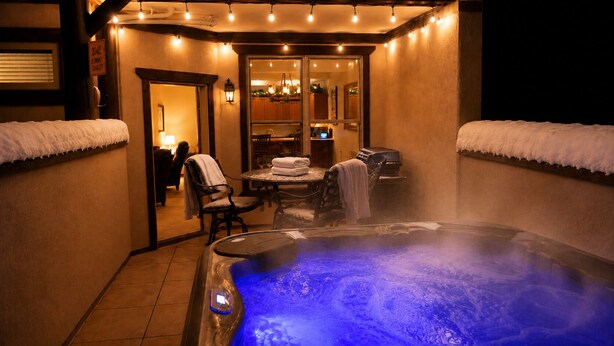 A hot tub with a blue light, a table with chairs, and a door leading to a room.