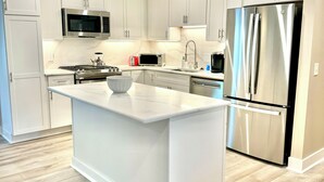 A modern kitchen with white cabinetry, a stainless steel refrigerator, and a central island. - Cute Cottage 3 Blocks to Beach & Village! BRAND NEW remodel Fall of 2024! (Saint Simons Island)