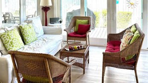 A sunlit room with wicker furniture, a white sofa, and a table with fruit. - Cute Cottage 3 Blocks to Beach & Village! BRAND NEW remodel Fall of 2024! (Saint Simons Island)