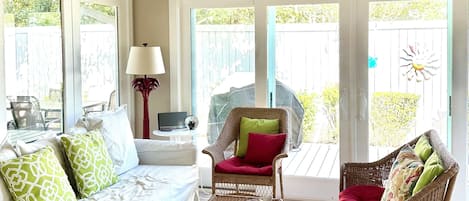 A sunlit room with wicker furniture, a white sofa, and a table with fruit.