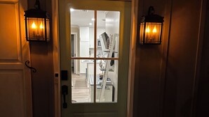 A front door with a glass panel, two wall-mounted lanterns, and a visible interior hallway leading to a kitchen area. - Cute Cottage 3 Blocks to Beach & Village! BRAND NEW remodel Fall of 2024! (Saint Simons Island)