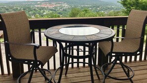 Een ronde tafel met vier stoelen op een houten terras, met uitzicht op een schilderachtig landschap met heuvels en gebouwen.