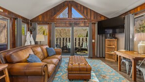 A spacious living room with a brown leather sofa, a wooden coffee table, and a large window overlooking a deck.