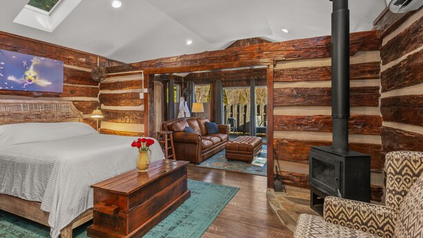 A log cabin interior with a bed, sofa, ottoman, and a fireplace.