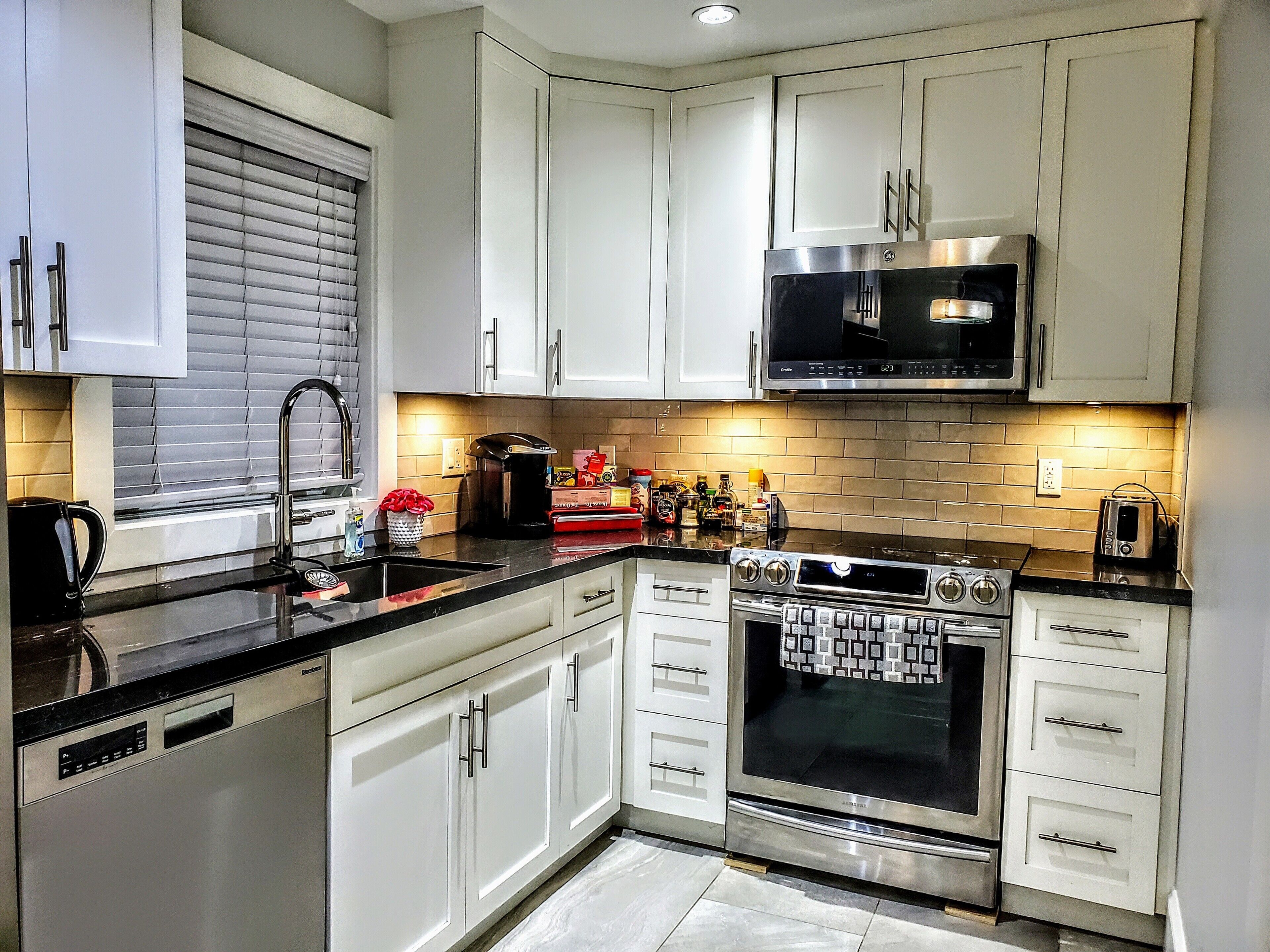 Una cocina moderna con armarios blancos, una estufa de acero inoxidable, un microondas y un tostador.