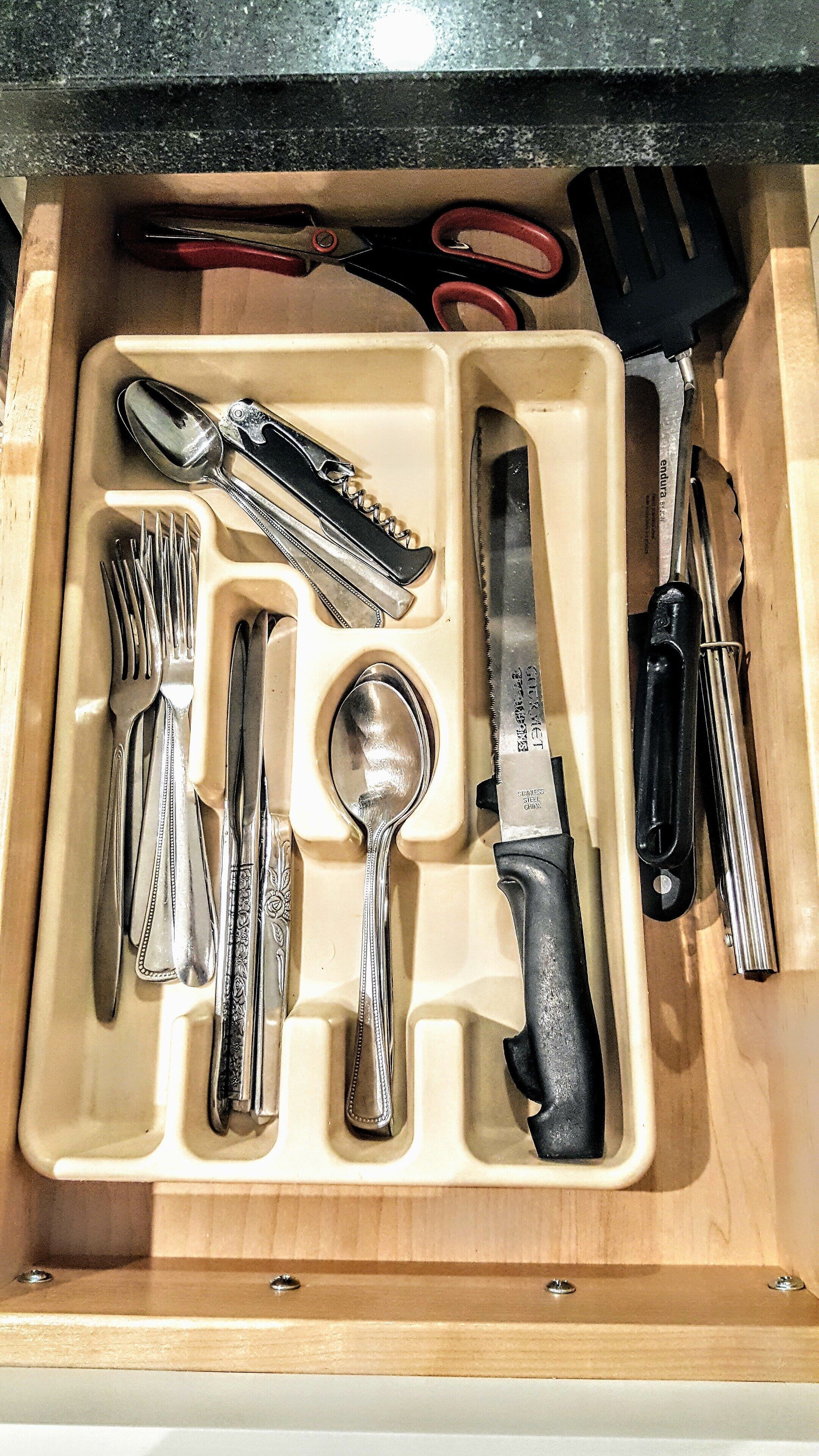 A drawer with compartments containing various kitchen utensils including forks, knives, a spoon, and a grater.