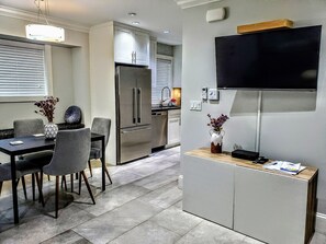 Une cuisine moderne dotée d’un réfrigérateur encastré, d’un coin repas avec une table et des chaises, et d’un téléviseur à écran plat fixé au mur.