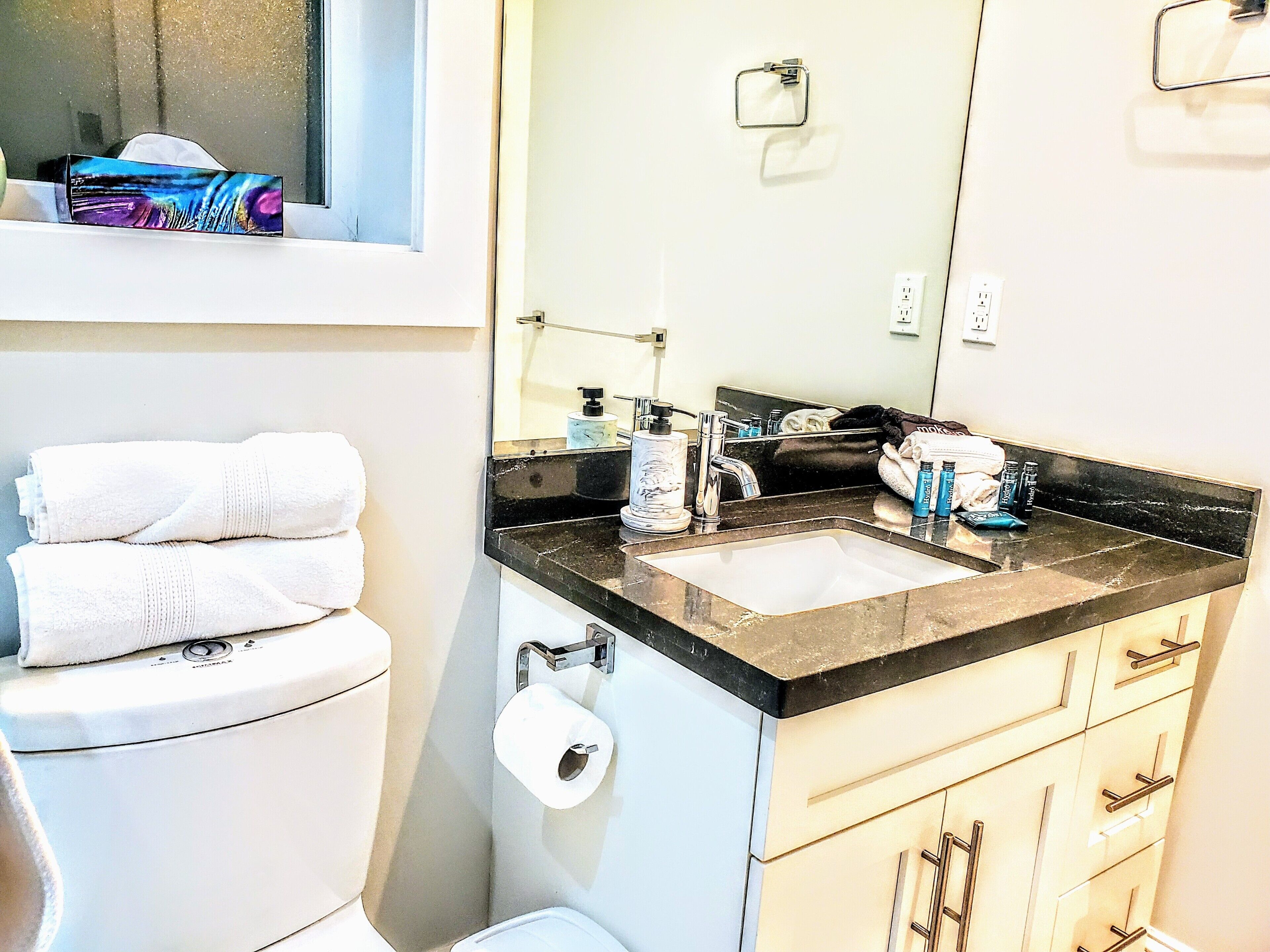 A bathroom with a toilet, a sink, a mirror, and a window.
