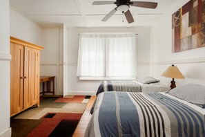 A bedroom with a bed, a wooden wardrobe, a window with curtains, a ceiling fan, and a lamp.