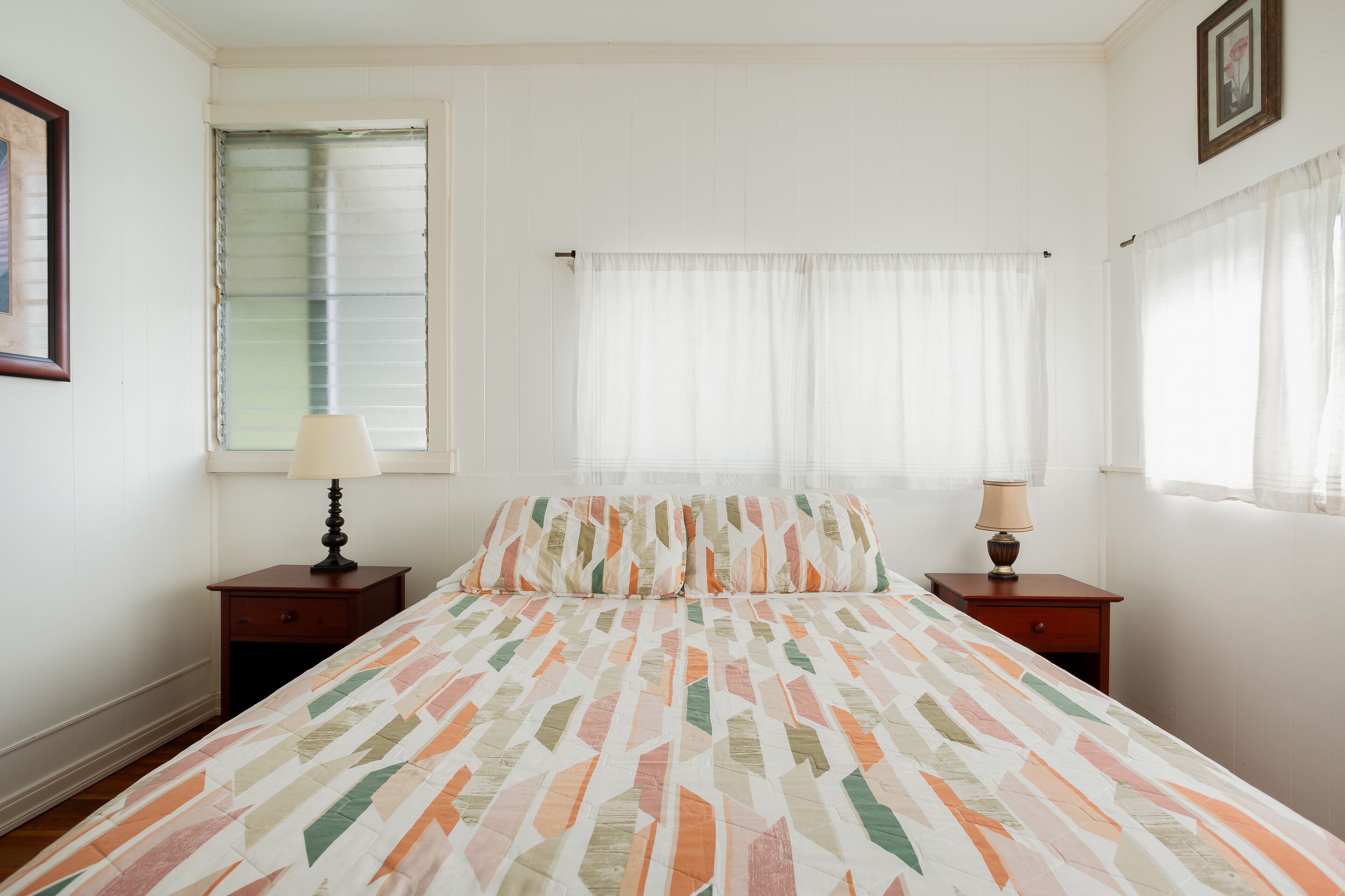 A bedroom with a bed, two nightstands, a window with blinds, and a picture on the wall.