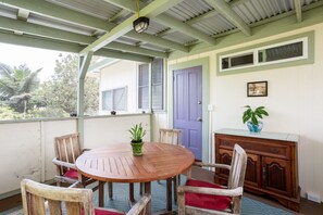 A covered outdoor area with a wooden table and chairs, a purple door, and a cabinet with a plant on top.