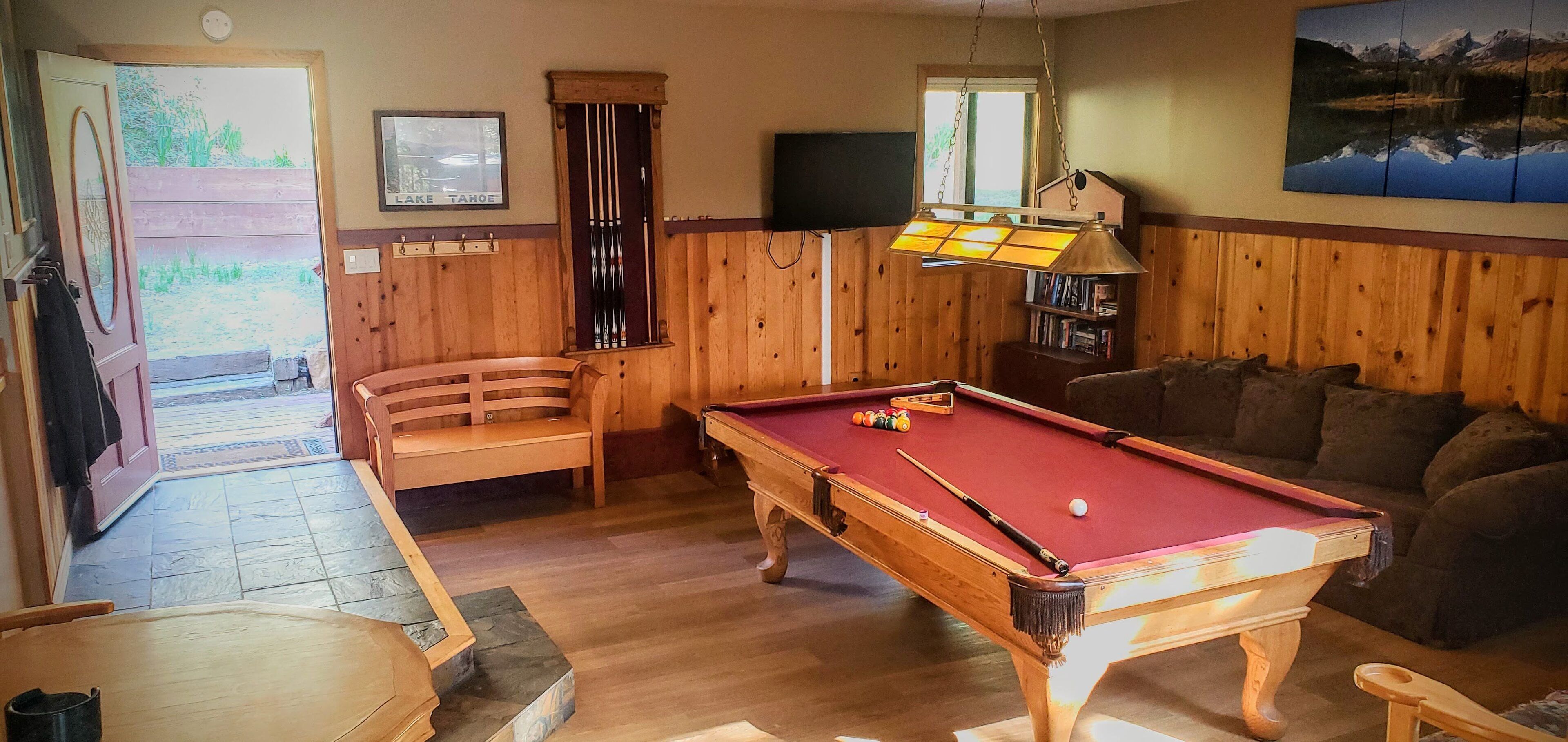 A pool table in a room with wooden walls, a sofa, and a door leading outside.