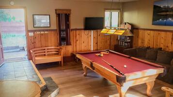 A pool table in a room with wooden walls, a sofa, and a door leading outside.
