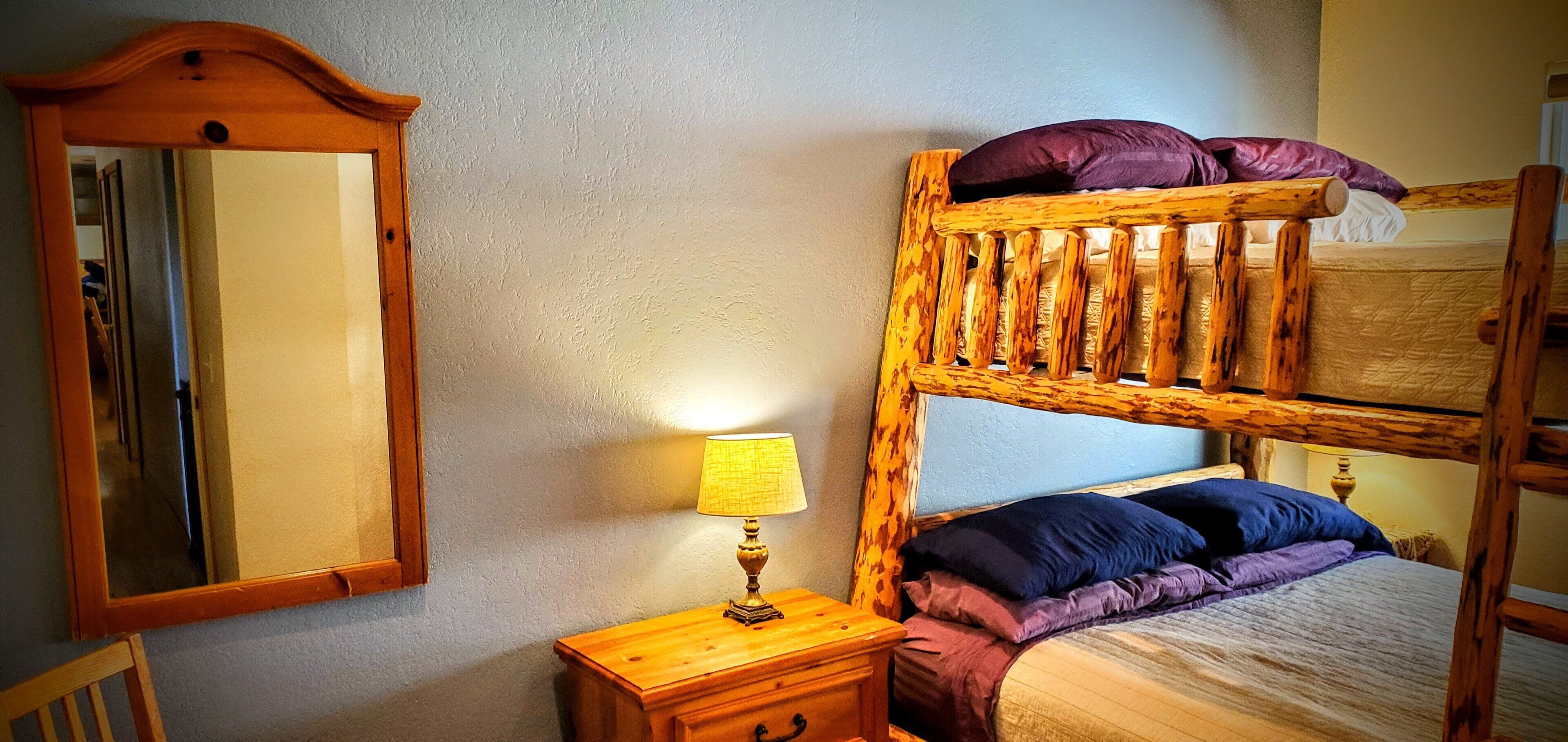 A bunk bed with a wooden headboard, a bedside table with a lamp, and a mirror on the wall.