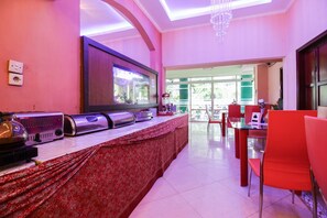 A modern kitchen with a large flat-screen TV, a coffee machine, and a microwave. There is a dining area with red chairs and a table.