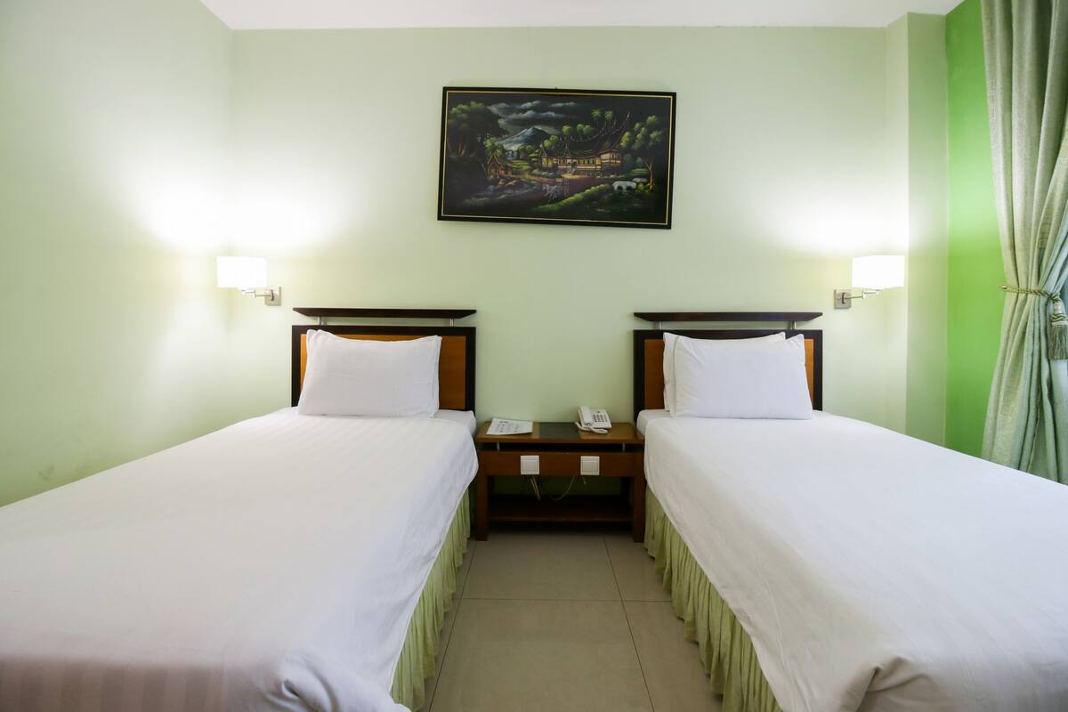Ein Hotelzimmer mit zwei Einzelbetten, einem Nachttisch mit Telefon und einem Bild an der Wand.