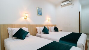 Ett hotellrum med två separata sängar, var och en med en vit madrass, gröna kuddar och ett mörkgrönt täcke. Det finns väggmonterade lampor och en luftkonditioneringsanläggning ovanför sängarna.