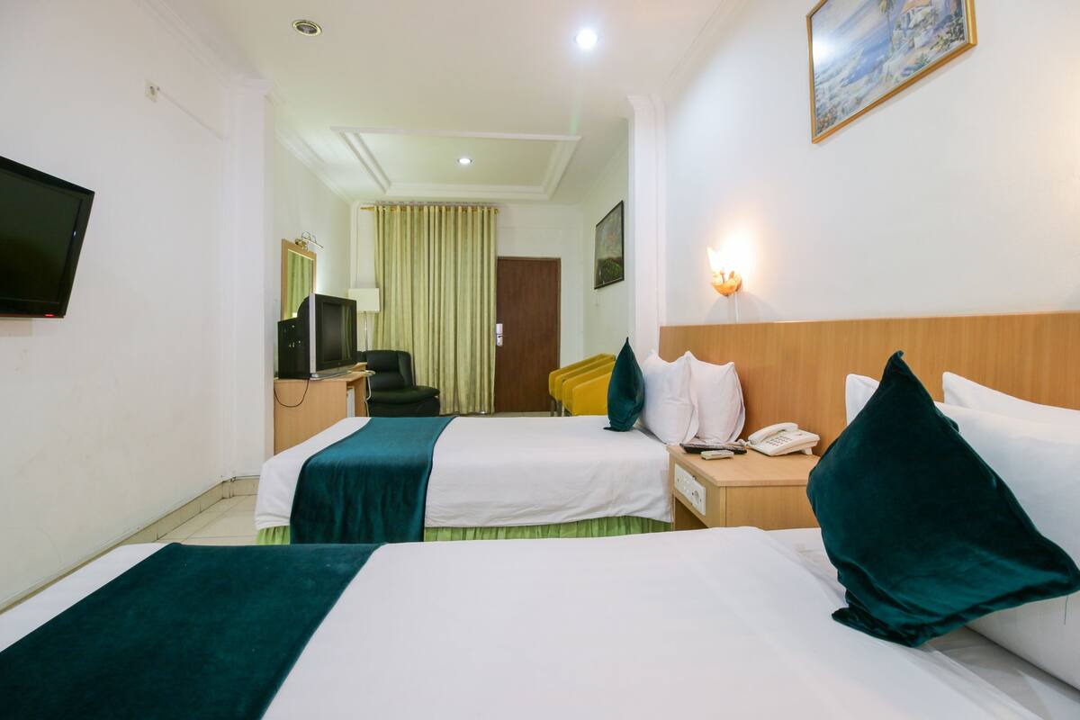 Ein Hotelzimmer mit zwei Betten, einem Schreibtisch, einem Stuhl, einem Fernseher und einem Gemälde an der Wand.