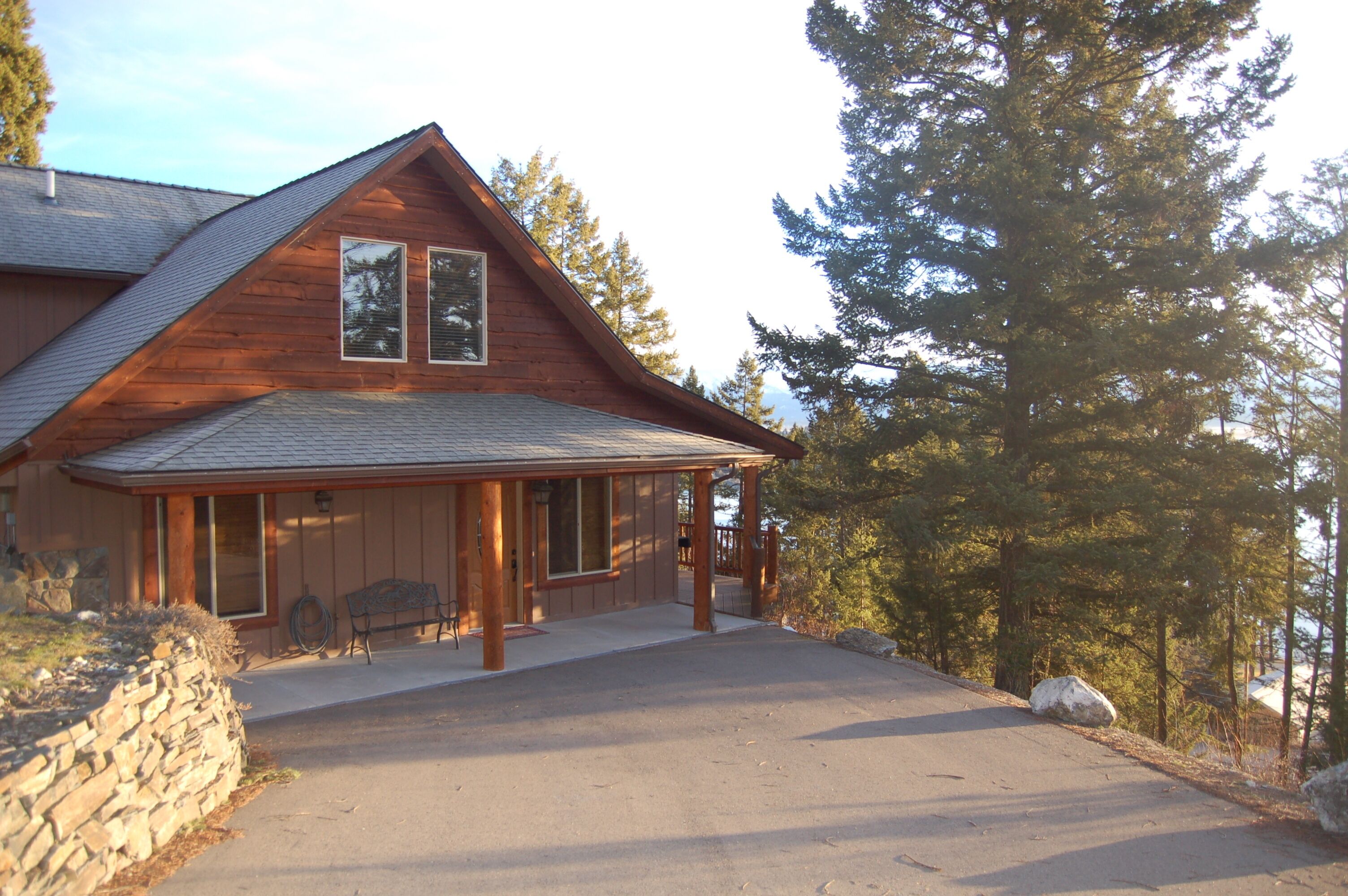 A wooden cabin with a sloped roof, large windows, and a stone wall in front.
