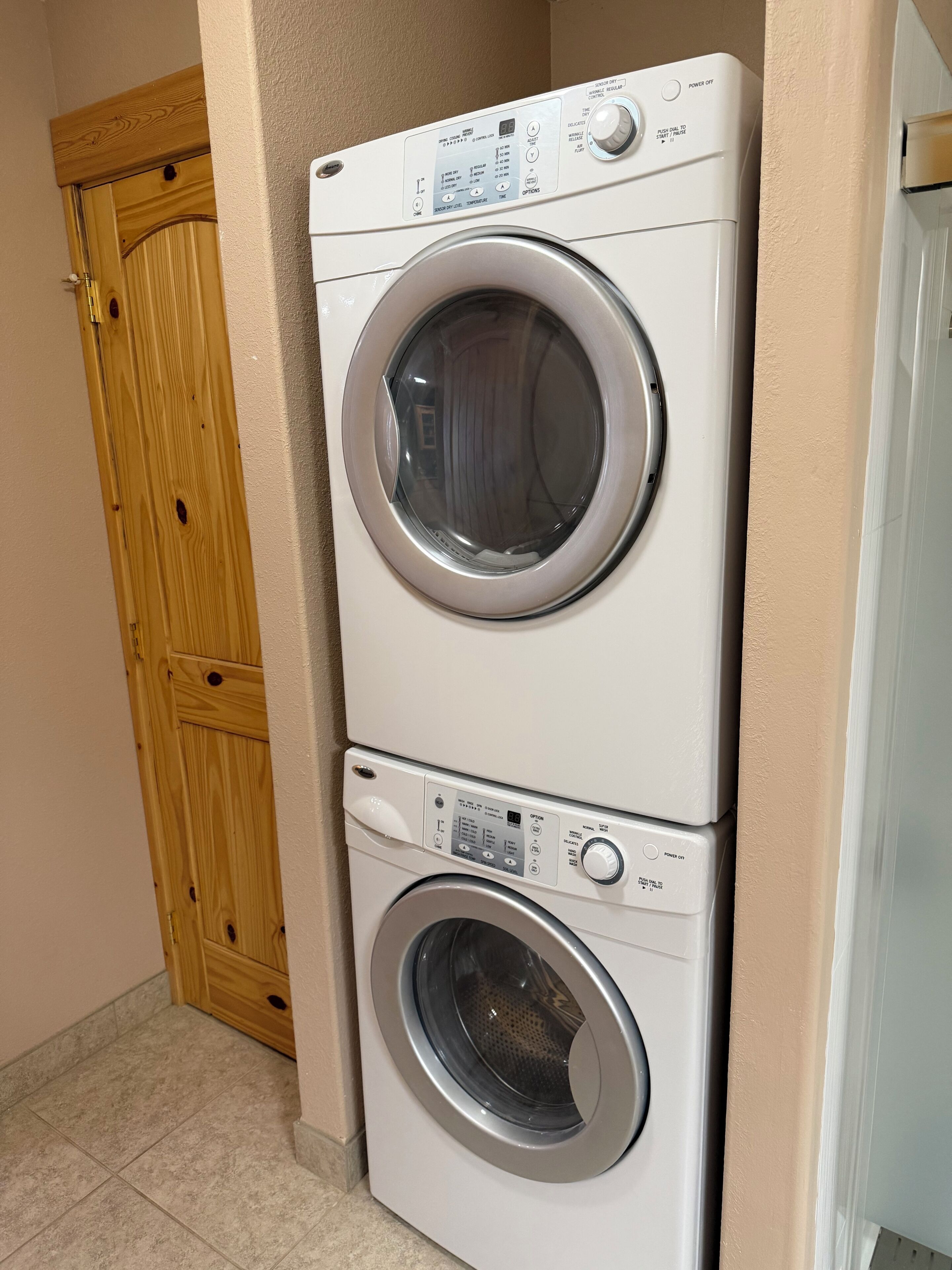 Eine übereinander gestellte Waschmaschine und ein Trockner in einer Diele mit Holztür und Fliesenboden.