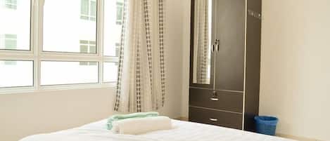 A hotel room with a bed, a wardrobe, a window with curtains, and a view of buildings outside.