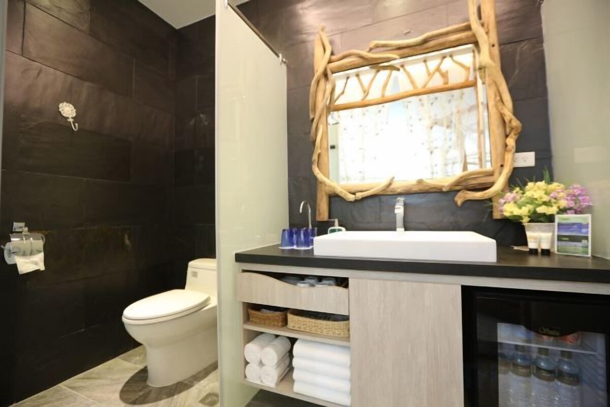 A bathroom with a dark wood wall, a white toilet, a wooden-framed mirror, a sink, and a shelf with towels.