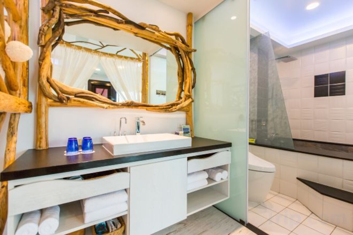 A bathroom with a wooden-framed mirror, a white sink, and a glass shower enclosure.